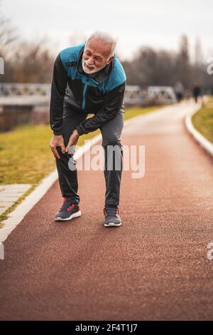 Active senior man is having pain in knee while jogging. Stock Photo