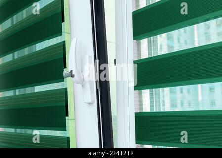 Metal plastic windows with blinds, close up view on handle with a lock. The concept of protecting a child from falling out of windows. Details of emerald roller blinds. Child safety at home concept Stock Photo