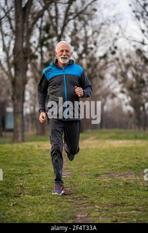Happy senior man is jogging in park. Stock Photo