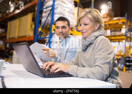 workers in open warehouse office using laptop Stock Photo