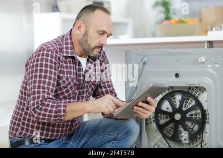 man looking at tablet by broekn down washing machine Stock Photo
