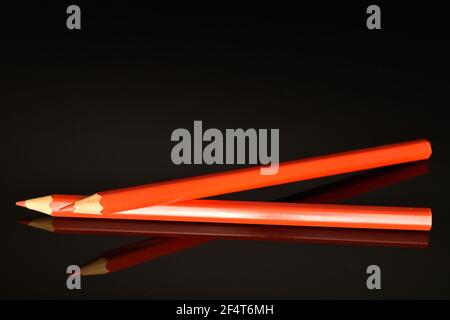 Two red colored office pencils, close-up, on a black background. Stock Photo