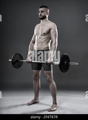 Young athletic man training with a barbell isolated on gray background Stock Photo