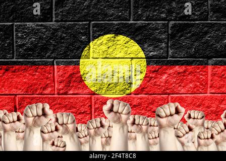 Raised fists against the background of the depicted flag of Australian Aboriginal on a brick wall, a concept of strength and unity.