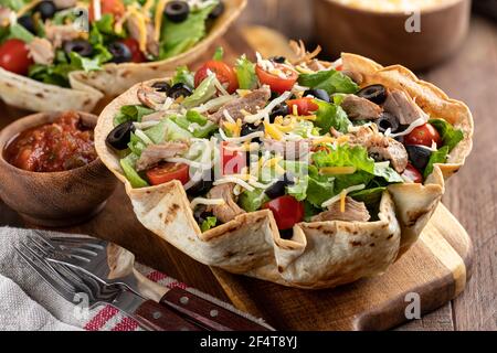 Taco salad with tomato, lettuce, black olives, cheese and pork in a tortilla shell on a wooden board Stock Photo