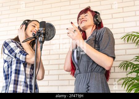 From below glad young woman smiling and listening to music in headphones while standing near microphone in recording studio Stock Photo