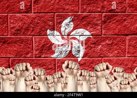 Raised fists against the background of the depicted flag of Hong Kong on a brick wall, a concept of strength and unity. Stock Photo