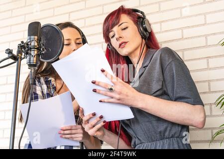 From below young female hostesses reading script before recording radio podcast in studio Stock Photo