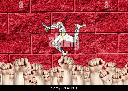 Raised fists against the background of the depicted flag of Isle Of Man on a brick wall, a concept of strength and unity. Stock Photo