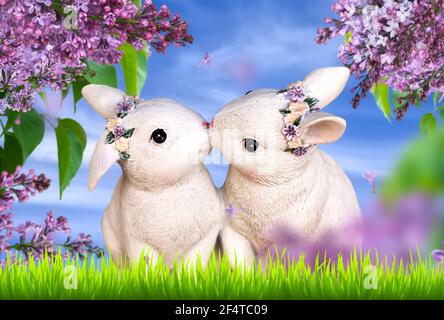 Two white hare figures on a meadow framed with lilac branches. Beautiful Easter card Stock Photo
