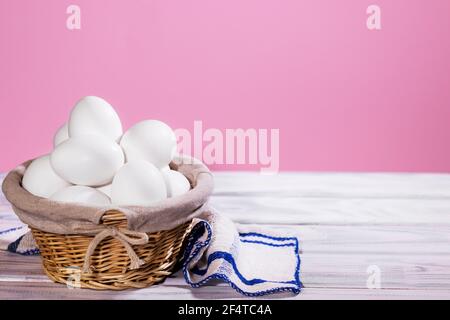 White Chicken eggs in a Straw basket on a pink background with piece of cloth, Natural Product Stock Photo