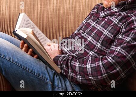 MANCHESTER, UNITED KINGDOM - Mar 21, 2021: Man sat in a chair reading a book blue jeans and a check shirt casually dressed Stock Photo