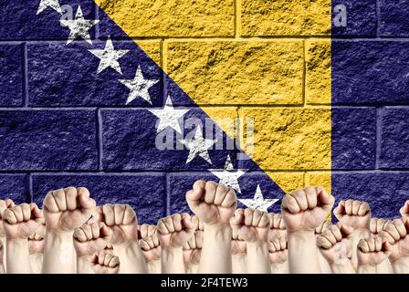 Raised fists against the background of the depicted flag of Bosnia and Herzegovina on a brick wall, a concept of strength and unity. Stock Photo