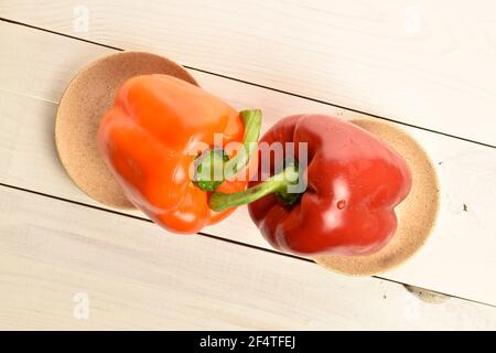 Two whole organic fresh juicy tasty bell peppers, close-up, on two ceramic saucers, standing on a painted white natural wood worktop. Stock Photo