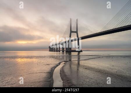 Background with colourful sunrise on the Lisbon bridge. The Vasco da Gama Bridge is a landmark, and one of the longest bridges in the world. Urban lan Stock Photo