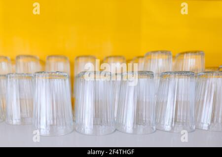 Clean glassware neatly arranged on open shelve with yellowish background Stock Photo