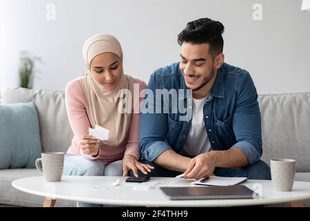 Smiling man and woman in hijab working on family budget Stock Photo