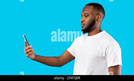 Black Man Scanning Face Using Phone Standing Over Blue Background Stock Photo