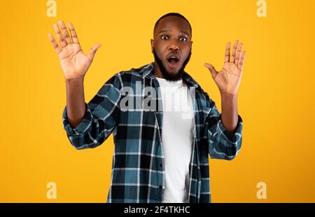 Shocked African American Guy Raising Hands Posing Over Yellow Background Stock Photo