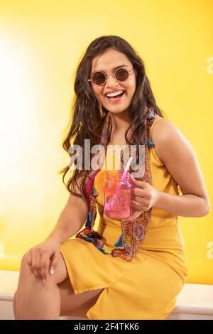 A STYLISH YOUNG WOMAN LAUGHING WHILE SITTING WITH A DRINK IN HAND Stock Photo