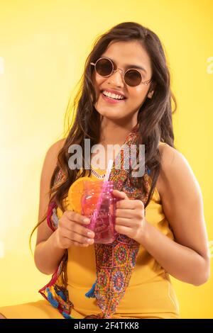 A CHEERFUL YOUNG WOMAN POSING IN FRONT OF CAMERA WITH FRUIT DRINK IN HAND Stock Photo