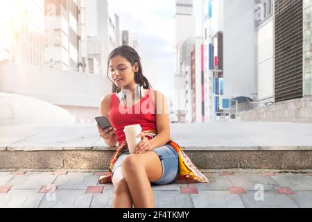 A STYLISH YOUNG WOMAN SITTING OUTSIDE AND USING MOBILE PHONE Stock Photo