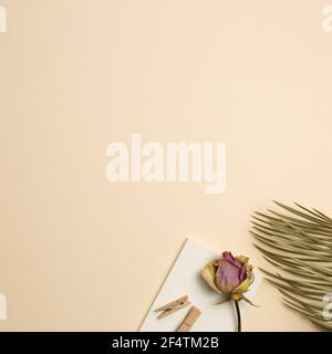 Notebook, wooden clip, dry rose and leaf on beige background. flat lay, top view, copy space Stock Photo