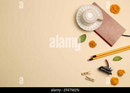 Notebook, mug cup, pencil, stapler, clip, dry flowers on beige background. flat lay, top view, copy space. Work and study place Stock Photo