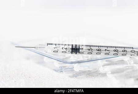 Glass medical ampoules on the table in a transparent package and a syringe on ampoules on a white background. Medical vial and syringe close-up. Stock Photo