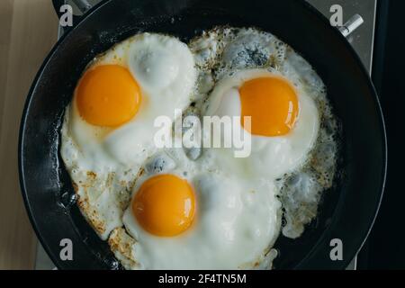 Keto meal eggs frying on hot cast iron frying pan, three fried yellow yolk, ketogenic diet Stock Photo