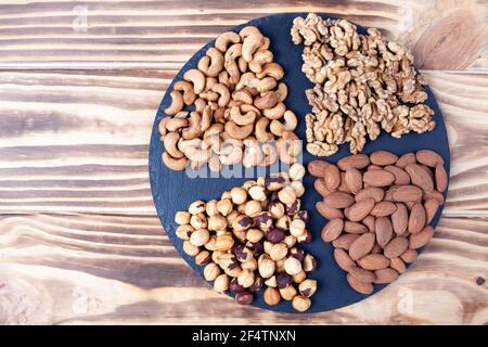 Various nuts sorted in glass bowl with honey bowl and honey dipper. Mixed nuts on wooden table. Black stone plate on wooden background. Stock Photo