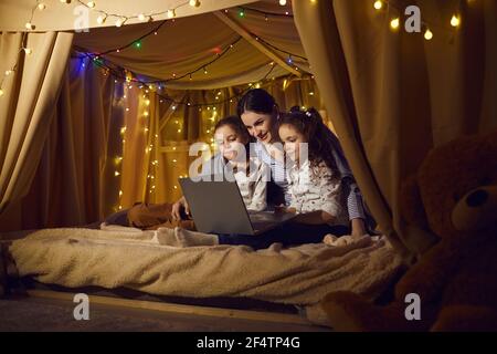 Mother with preschool daughters watching movie on laptop in kids tent at home Stock Photo