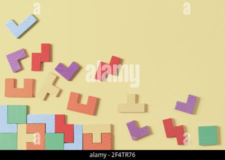Different colorful shapes wooden puzzle blocks on yellow background. Geometric shapes in different colors, top view Stock Photo