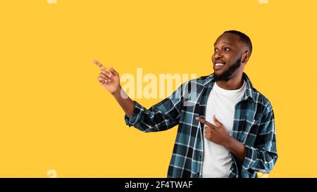 Positive Black Man Pointing Fingers Aside Standing Over Yellow Background Stock Photo