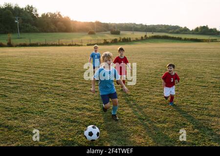 Children playing soccer. Cheerful boys in football dresses running after ball on field. Stock Photo