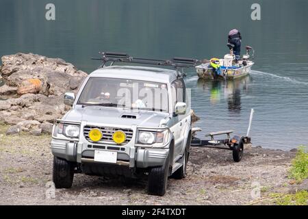 The car with a trolley for transit a boat on the shore of the lake, in the background a man prepares a vessel Stock Photo