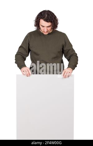 Young man, long curly hair style, looks down as holds a blank banner or placard, isolated on white background. Thoughtful student guy with a copy spac Stock Photo