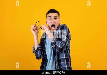 Horrified young guy yelling in panic, taking off his glasses over orange studio background Stock Photo