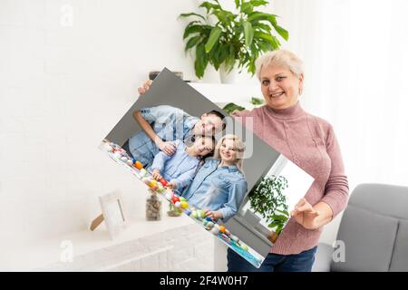 A happy blonde woman is holding a large wall canvas portrait of her family with young children. Stock Photo