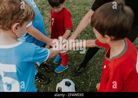Soccer players and referee standing around ball stacking hands. Group of children in red and blue football dresses and referee putting hands together.