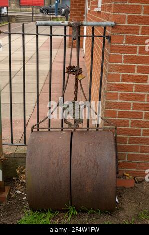 A old heavy garden roller chained to a metal fence Stock Photo