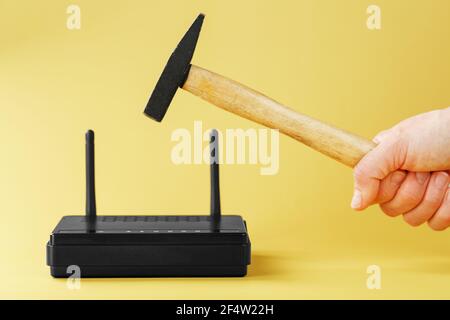 Hammer over the Wi-Fi router for destruction on a yellow background. Annoying internet with network connection destruction Stock Photo