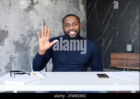 Video conference with a smart and smiling African-American male entrepreneur, virtual meeting with dark skinned employee. Webcam view of black guy waving hello in the camera, greeting interlocutor Stock Photo