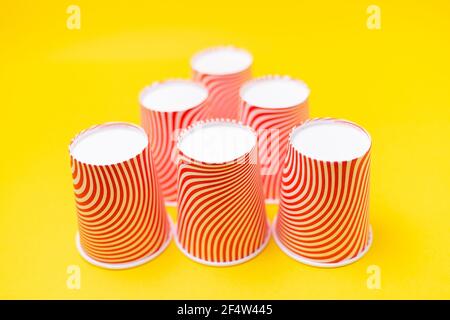 A pyramid of striped red paper cups, on a yellow background. Copy space ...