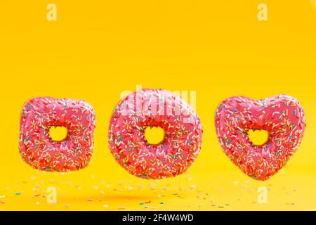 Three doughnuts of different shapes, with pink icing, on a yellow background. Copy space. Stock Photo