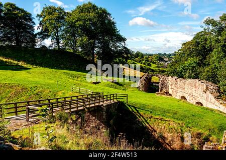 A picturesque view from the wooden moat  bridge of Norham Castle across the gate in the curtain wall and rolling green hills to Norham village Stock Photo