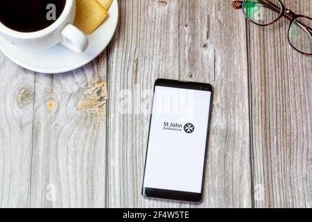 A mobile phone or cell phone laid on a wooden table with the St John ambulance first aid app open on screen Stock Photo