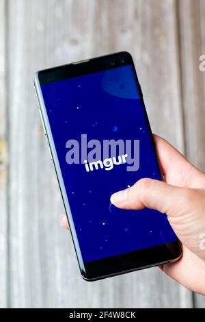 A mobile phone or cell phone being held in a hand with the Imgur app open on screen Stock Photo