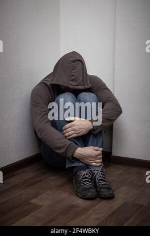 desperate young drug addict wearing hood and sitting alone in corner. concept of sadness, depressed and life problems Stock Photo