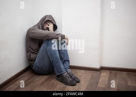 desperate young drug addict wearing hood and sitting alone in corner. concept of sadness, depressed and life problems Stock Photo